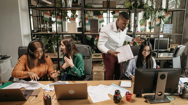 A diverse team of call center agents in a lively office setting, collaborating on tasks and discussing reports.