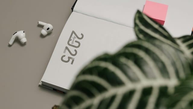 Open 2025 planner with AirPods and sticky notes, creating a modern workspace vibe.
