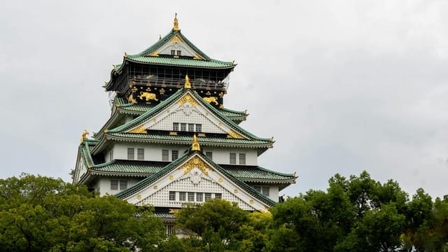 Stunning view of Osaka Castle surrounded by lush greenery under a cloudy sky, epitomizing traditional Japanese architecture.