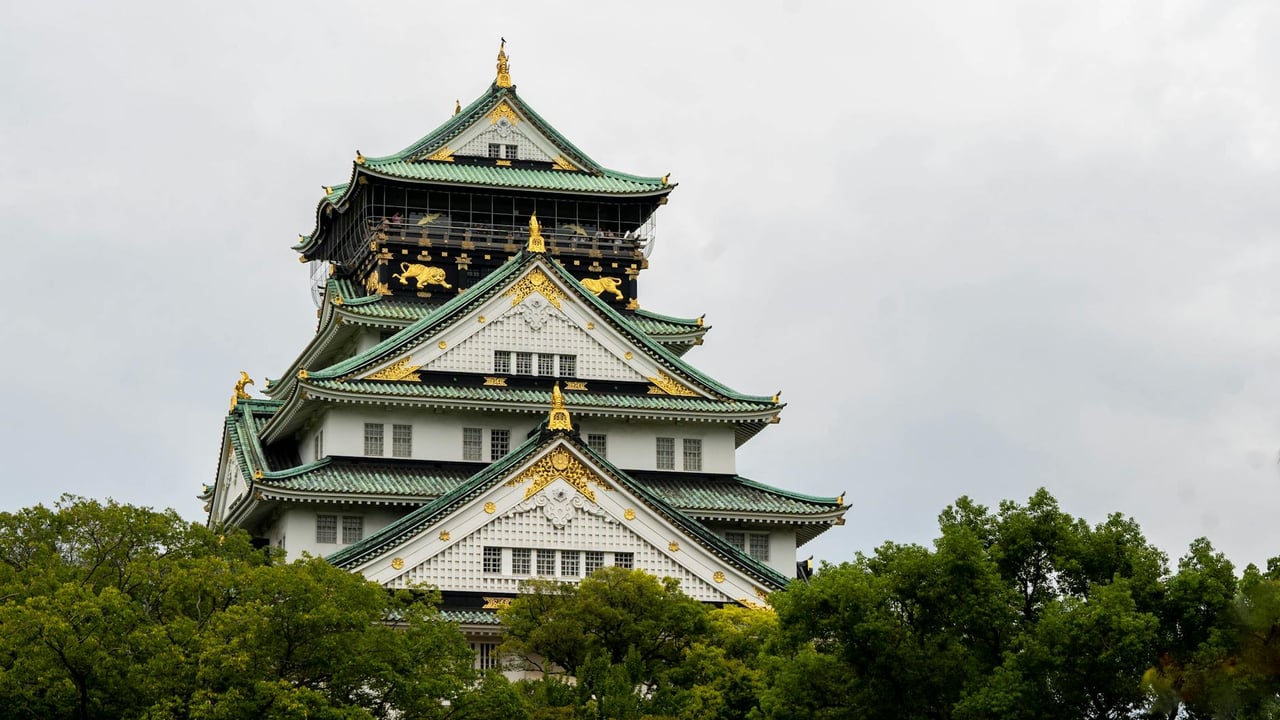 Stunning view of Osaka Castle surrounded by lush greenery under a cloudy sky, epitomizing traditional Japanese architecture.