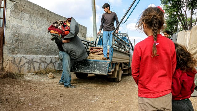 Men and children witness aid delivery in Idlib, Syria, highlighting refugee life.