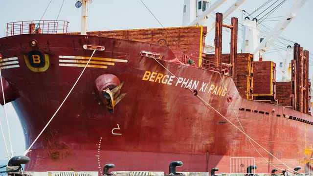 Close-up view of a large red cargo ship named Berge Phan Xi Pang docked at a port.