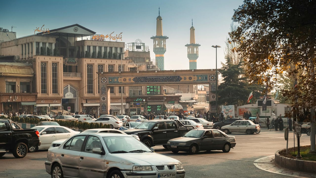 Bustling Tehran street scene with cars, mosque minarets, and traditional architecture.
