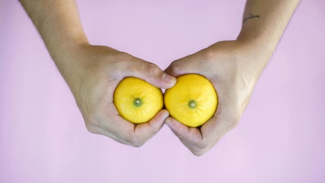 Creative concept with hands holding two lemons against pink background.