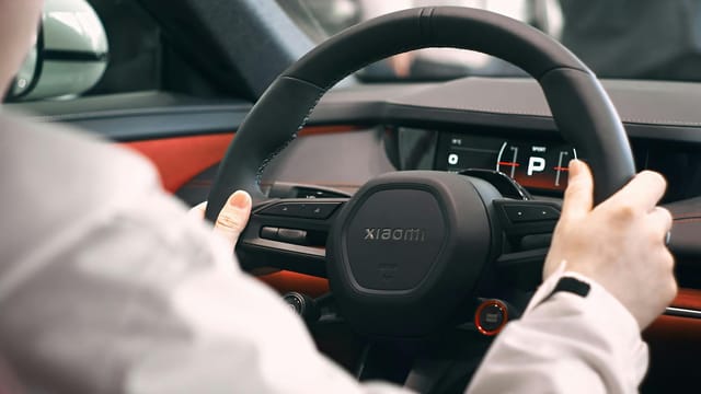 Close-up view of a person holding a steering wheel inside an electric car, focusing on the dashboard.