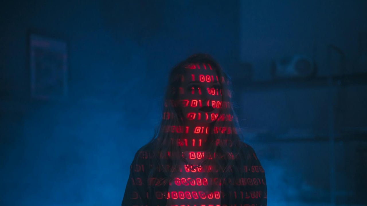 A mysterious silhouette with red binary code projected over the face, set against a dark, moody background.