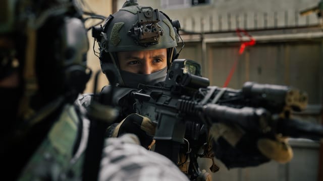 Focused soldier in tactical gear aiming rifle during an outdoor operation.