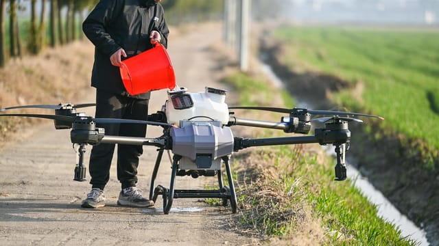 Person using a drone for agricultural purposes on a countryside pathway in Hefei, China.