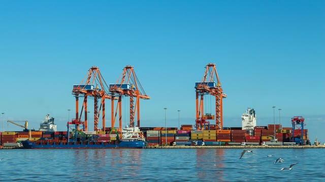 Illustrative image: Colorful container port with large cranes and ships against a clear blue sky.