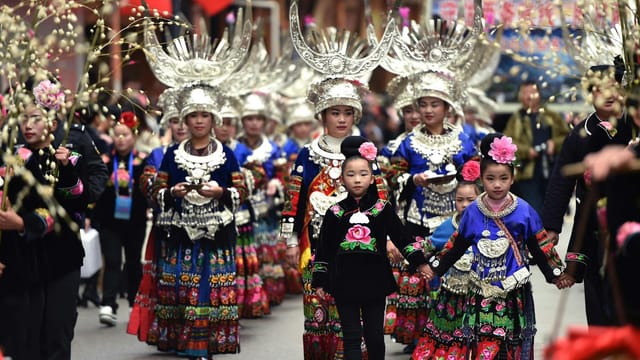 People in traditional Chinese clothing parade during a cultural festival, showcasing vibrant attire and elaborate headpieces.