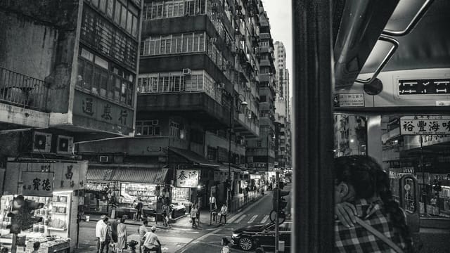 Black and white cityscape of busy streets in Hong Kong containing bustling modern architecture and people.