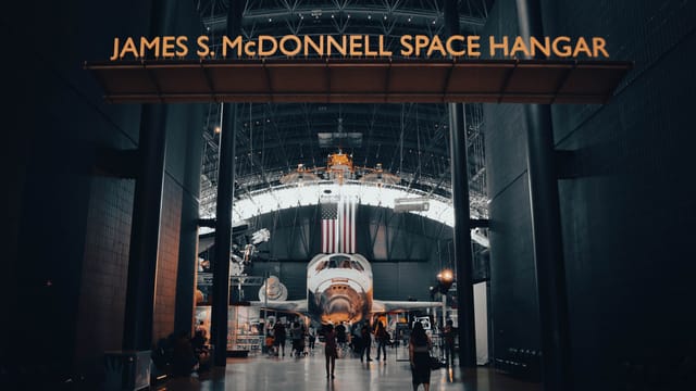 Interior view of the James S. McDonnell Space Hangar featuring a showcased spacecraft with visitors exploring.
