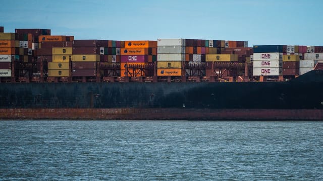 Illustrative image: Large cargo ship loaded with colorful containers on a calm sea under a clear sky.