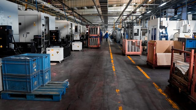 Illustrative image: Vast industrial factory floor with machinery, crates, and structured workstations.