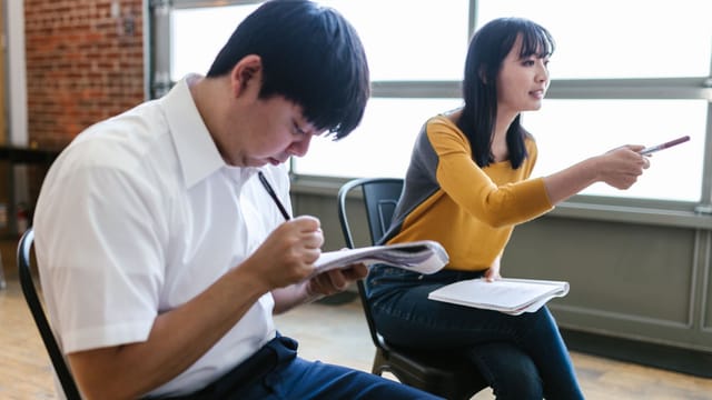Two adults engaged in an indoor workshop, taking notes and discussing ideas.