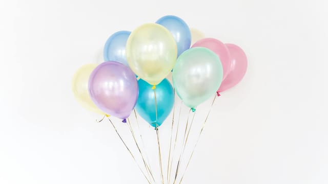 A cluster of colorful pastel balloons floating with a minimalistic white backdrop.