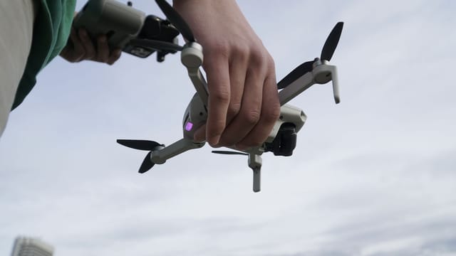 Close-up of a person holding a drone, ready for launch in an outdoor setting.