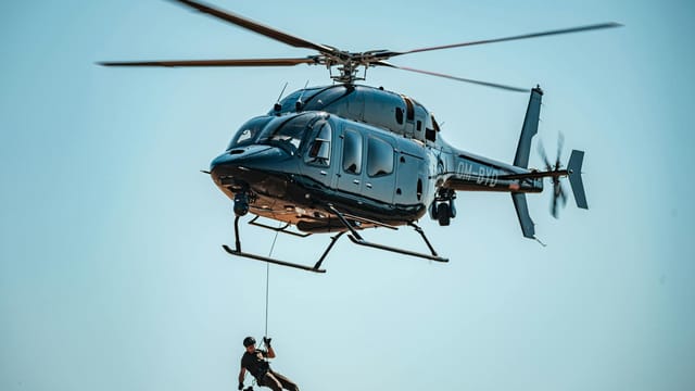 A man skillfully descends from a helicopter during a rescue operation in clear skies.