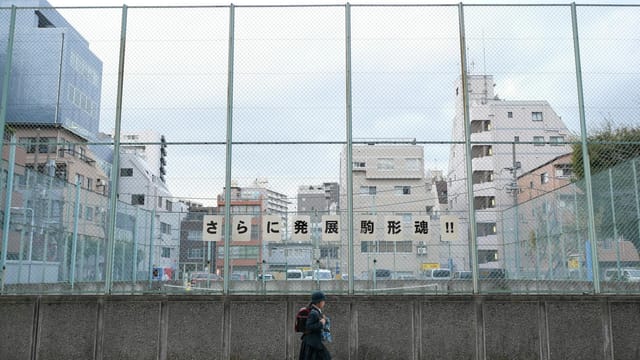 A schoolgirl walks along a fence in urban Tokyo, Japan.