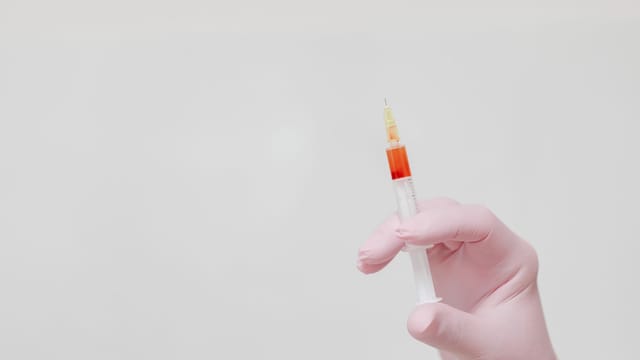 A gloved hand holding a syringe against a neutral background.