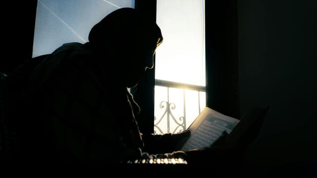 A silhouette of a person reading the Quran in Cairo, Egypt at sunset.