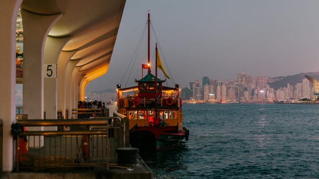 Vibrant ferry moored at Hong Kong harbor with city skyline and colorful twilight.
