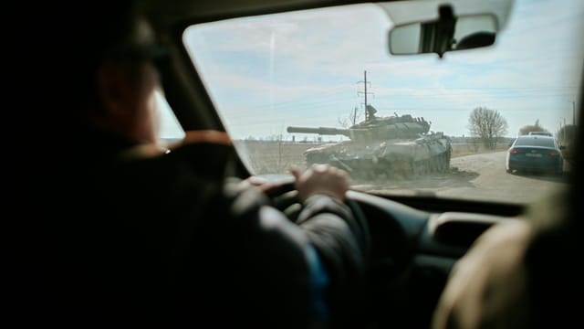 View from inside a car driving past a military tank on a road in Ukraine.