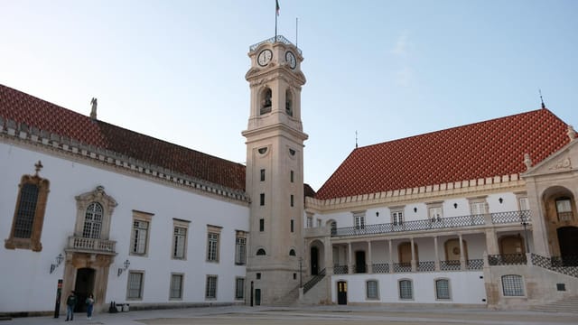 The iconic clock tower at the University of Coimbra, Portugal under a clear blue sky.