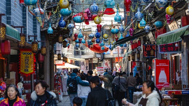A bustling outdoor market filled with colorful lanterns and people shopping on a sunny day.