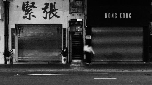Moody black and white photo capturing a quiet Hong Kong street with closed shopfronts.
