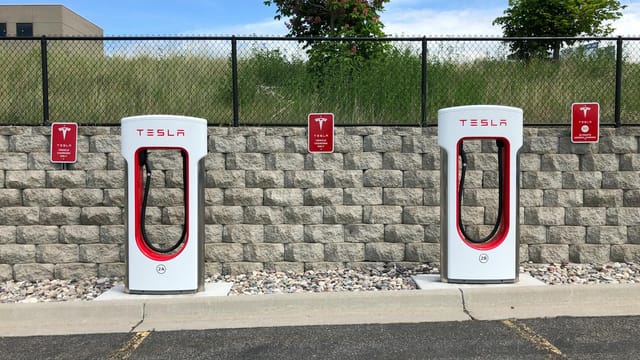 Dual Tesla electric car chargers in Idaho Falls parking lot with clear blue sky.