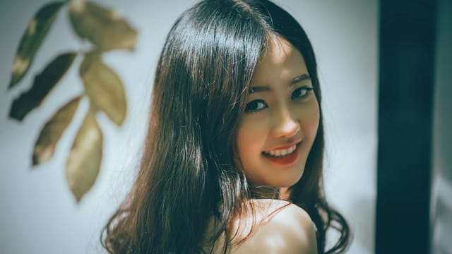 Portrait of a beautiful Asian woman with long hair smiling warmly, captured in an elegant studio setting.