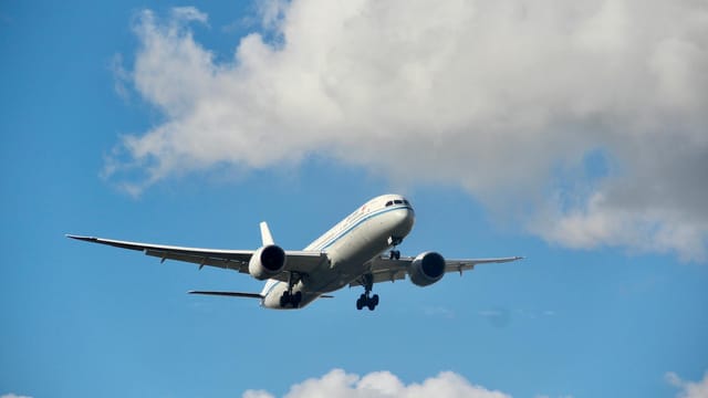 A commercial airplane soaring through a blue sky with fluffy clouds.