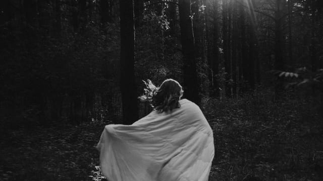 Enchanting black and white image of a woman in a light dress running through a sunlit forest.