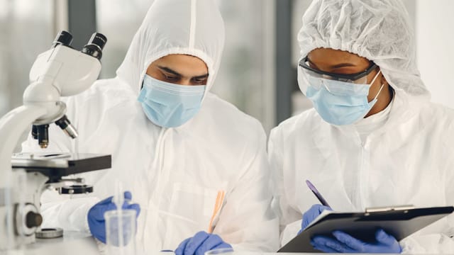 Two scientists in hazmat suits working with a microscope and notes in a laboratory setting.