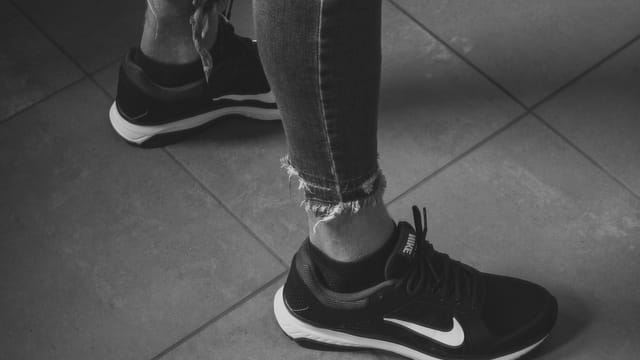 Close-up of a woman's legs wearing Nike sneakers and ripped jeans in monochrome style.
