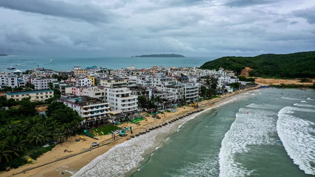 Drone captures vibrant Sanya coastline with beachfront buildings and lush greenery.