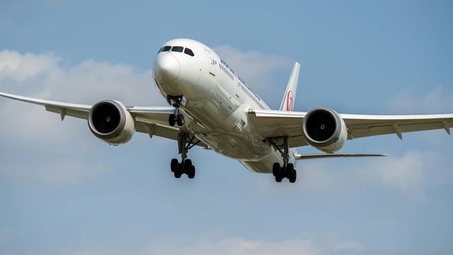 A white airplane flying low in the sky, showing front view of a jet aircraft with landing gear visible.
