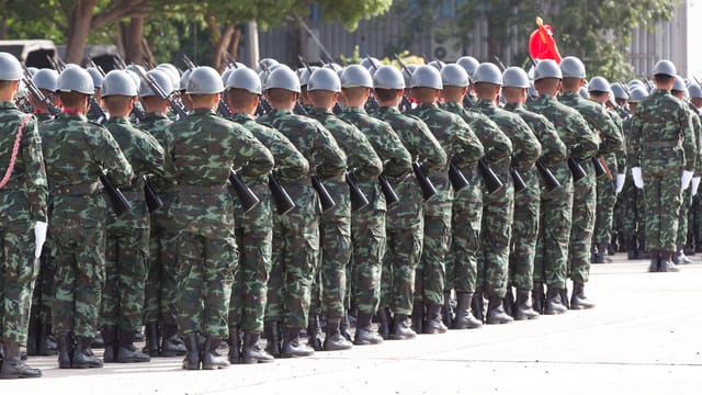 Back view unrecognizable soldiers with riffles wearing khaki uniform and hardhat lining up in rows during military ceremony