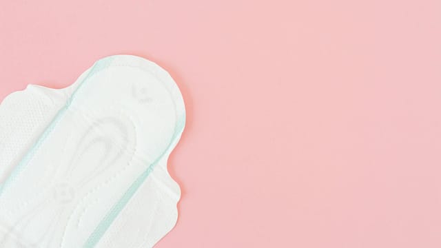 Close-up of a sanitary napkin on a pastel pink surface, offering copy space.