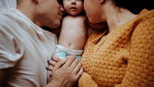 A tender family moment with parents embracing their infant in bed, showcasing love and intimacy.