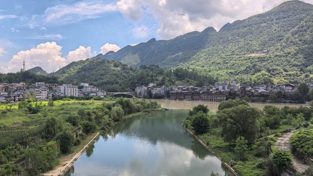 Idyllic landscape of a tranquil river, lush greenery, and mountains in Xiushan, China on a sunny day.