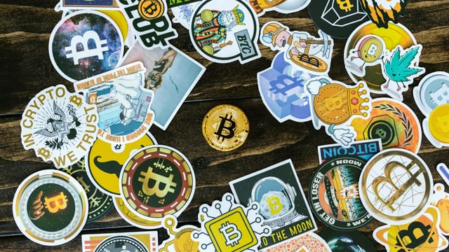 A collection of vibrant Bitcoin-themed stickers and a coin on a wooden surface. Ideal for cryptocurrency concepts.