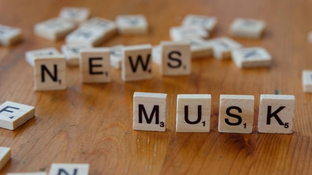 Close-up of wooden letter tiles on a table spelling 'News Musk', concept of media coverage.