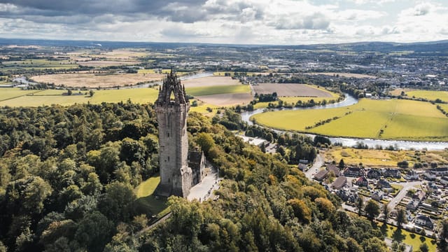 Majestic aerial view of The Wallace Monument surrounded by lush greenery and scenic landscapes in Stirling, Scotland.