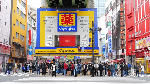 Crowd at a busy crosswalk in a vibrant Japanese city surrounded by colorful buildings and signage.