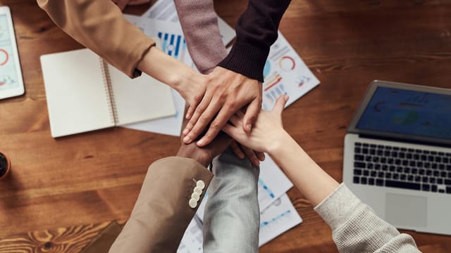 Diverse professionals unite for teamwork around a wooden table with laptops and documents.