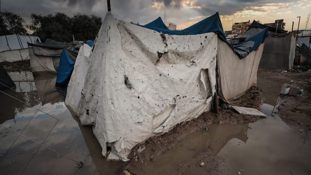 A damaged tent shelter in a flooded area of a Gaza refugee camp under stormy skies.