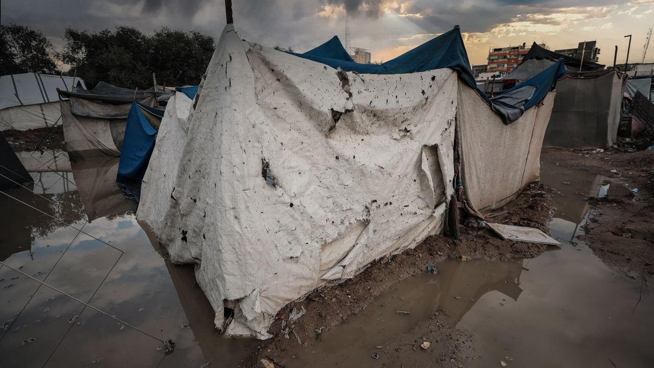 A damaged tent shelter in a flooded area of a Gaza refugee camp under stormy skies.