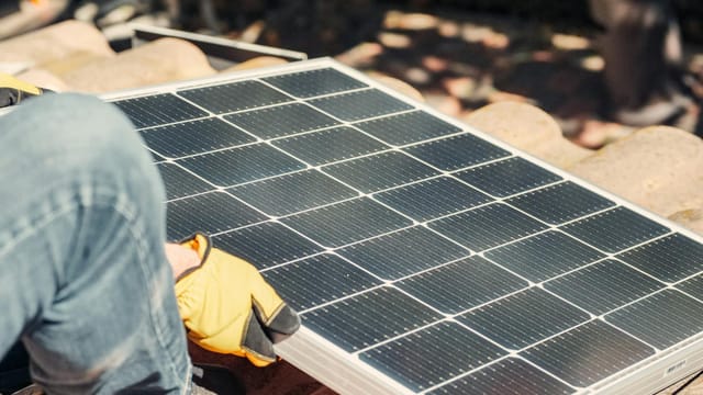 A worker installs a solar panel on a sunlit rooftop, exemplifying renewable energy.